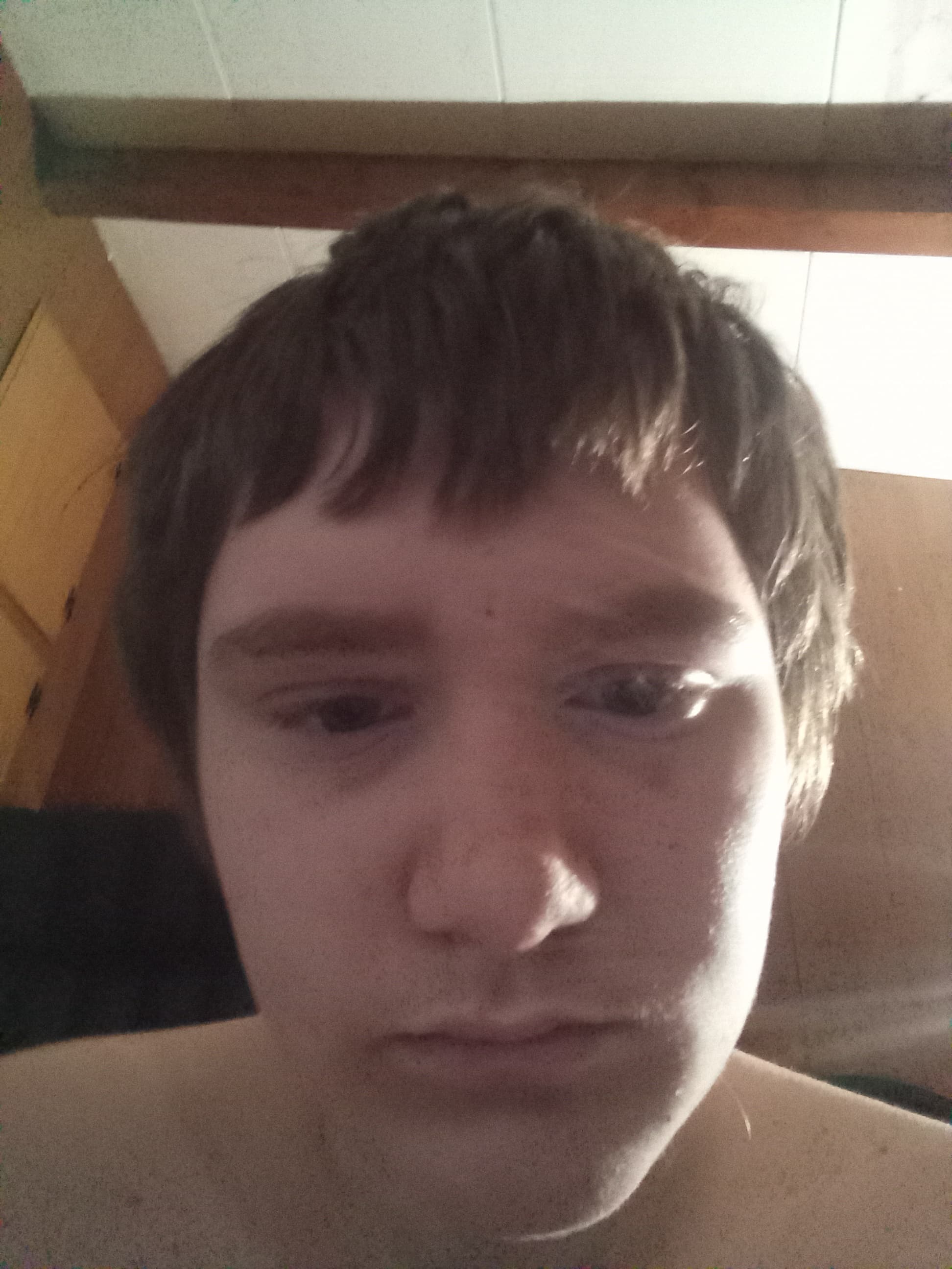 Close-up, angled selfie of a young person with short dark hair and a neutral expression.